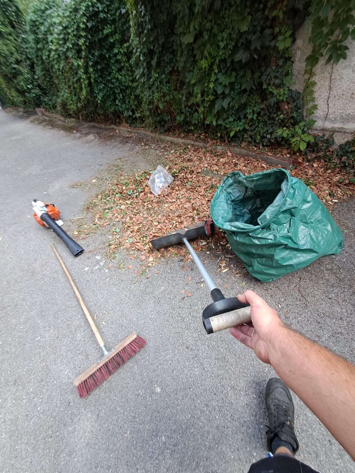 Zusammengekehrtes Laub mit Besen, Laubbläser und Sammelsack im Einsatz