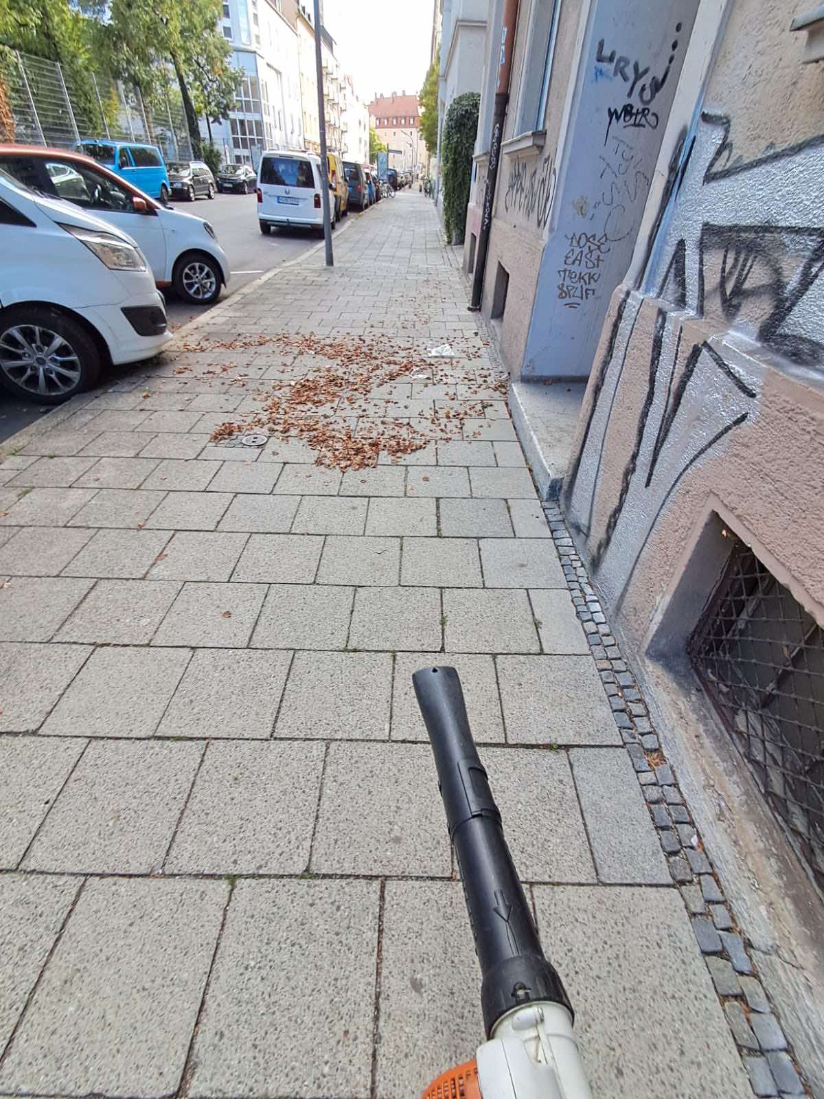 Laubbeseitigung mit Laubbläser auf dem Gehweg vor einem Wohngebäude